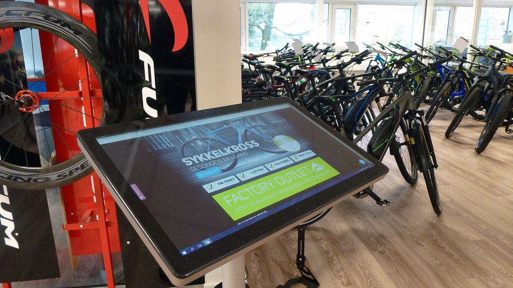 På dette bildet ser du to av de viktigste fremtidselementene til Meridastore.no. Berøringsskjermer i butikker og elsykler. - Elsykler blir bare viktigere og viktigere for sykkelbransjen, fastslår Stian Steen-Olsen.